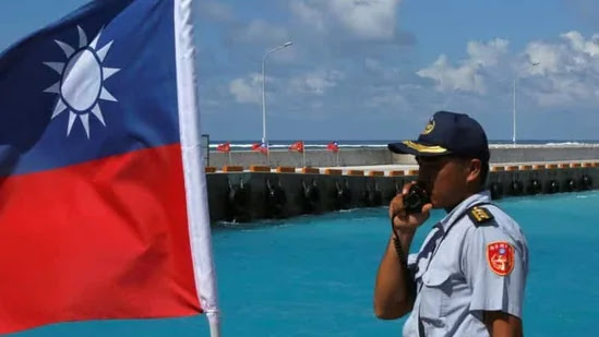 A member of the Taiwanese Coast Guard stands guard next to a Taiwanese flag on Itu Aba